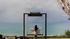A swing set with a sign that reads "THIS IS LIVING" and "Baja Verde" against a backdrop of a clear sky and ocean. - Beijo do Vento Pousada (Porto Seguro)