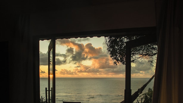 A bedroom with a large window overlooking the sea, a hammock, and a bed. - Beijo do Vento Pousada (Porto Seguro)