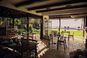 An outdoor dining area with tables and chairs, a view of the sea, and a thatched roof structure. - Beijo do Vento Pousada (Porto Seguro)