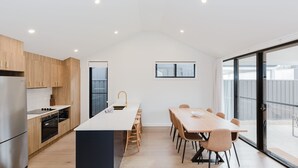 A modern kitchen with a central island, wooden cabinets, and a large window. - 16B Rawson Street - Brand new Build (Jindabyne)