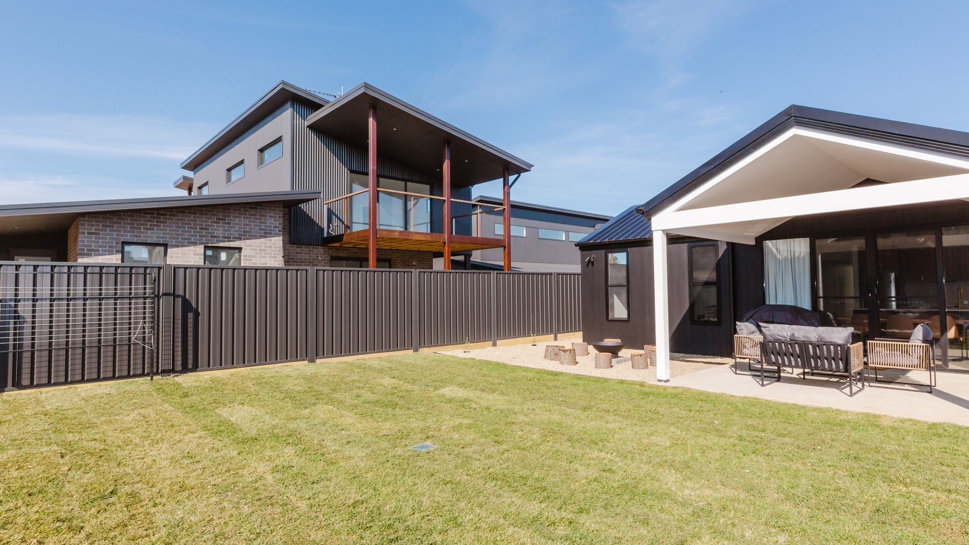 A modern two-story house with a covered patio area, a fenced backyard, and a visible outdoor seating arrangement.