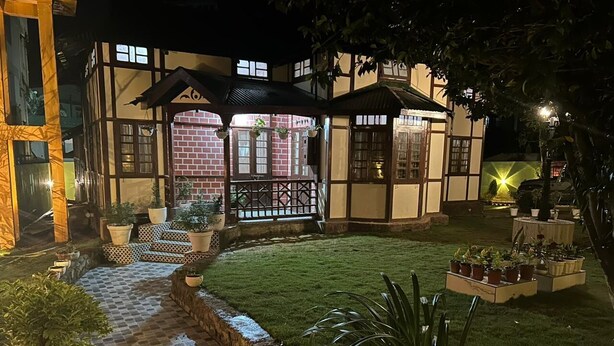 Una casa tradicional japonesa con un sendero de baldosas que conduce a un portón de madera, rodeada de plantas en macetas y un césped bien cuidado.
