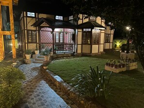 Una casa tradicional japonesa con un sendero de baldosas que conduce a un portón de madera, rodeada de plantas en macetas y un césped bien cuidado.