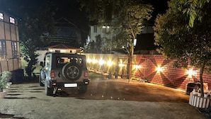 Un SUV estacionado en un área de estacionamiento tenuemente iluminada, con un muro de ladrillo y plantas en macetas.
