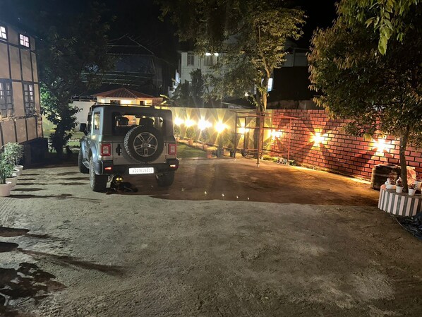 Un SUV estacionado en un área de estacionamiento tenuemente iluminada, con un muro de ladrillo y plantas en macetas.