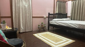 Un dormitorio con cama, una silla, una mesita con plantas en macetas y un tapete estampado.