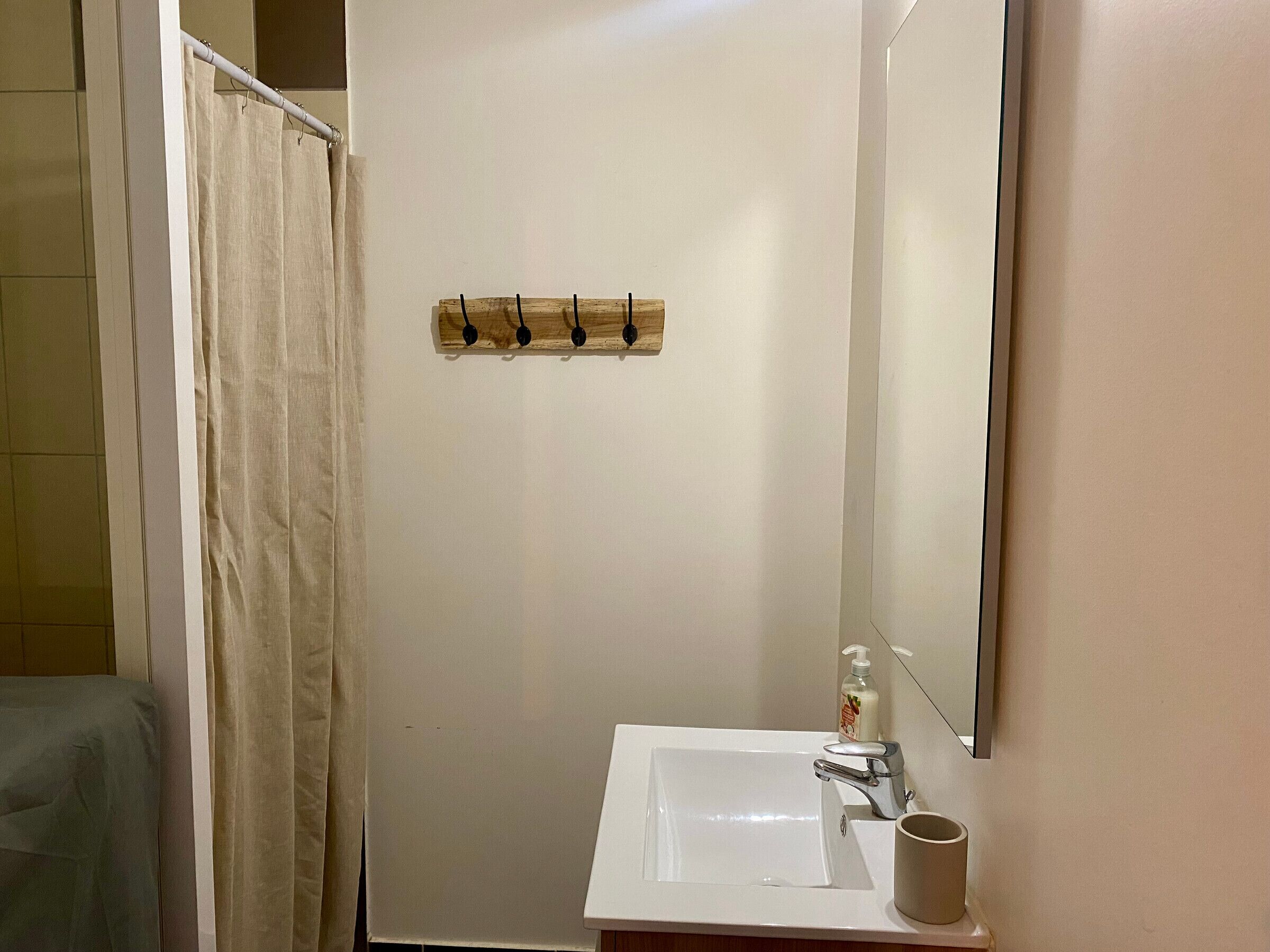 Ein Badezimmer mit weißem Waschbecken, einem Spiegel, einem Handtuchhalter und einer Duschvorhang.