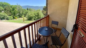 A balcony with a table and two chairs, a wooden railing, and a view of a green landscape with trees and mountains. - Cozy T2 Apartment for 3 in Formiguères - Close to Shops and Ski Slopes (Formiguères)