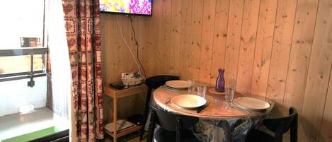 Un comedor con una mesa de madera, sillas y un televisor montado en la pared.