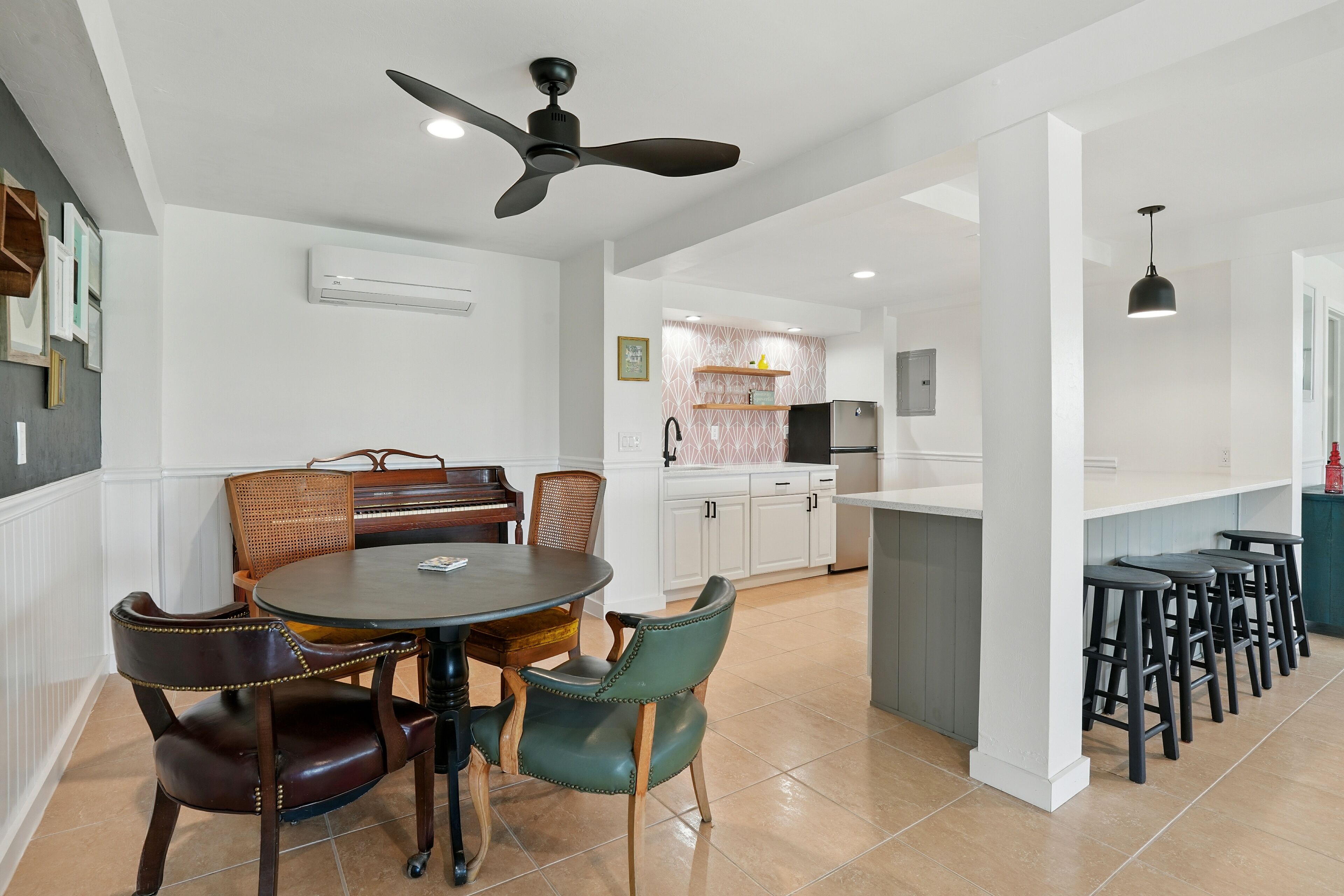 Une cuisine moderne avec des meubles blancs, un îlot central doté de tabourets et un ventilateur de plafond.