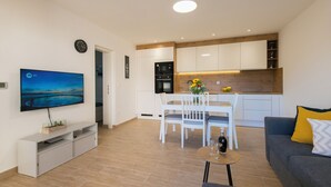 A modern living room with a flat-screen TV, a dining area with a white table and chairs, and a kitchen with white cabinets and wooden accents. - Apartment with Free Covered Parking (Zadar)