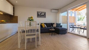 A modern living room with a sofa, dining table, and chairs. There is a kitchen area with cabinets and a fruit bowl. A world map is displayed on the wall. - Apartment with Free Covered Parking (Zadar)