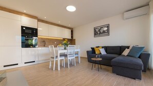 A modern kitchen with white cabinets, a dining table with chairs, and a grey sofa with cushions. - Apartment with Free Covered Parking (Zadar)