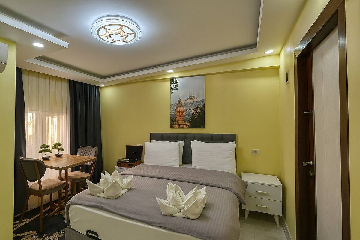 A hotel room with a bed, bedside table, chair, and a painting on the wall.