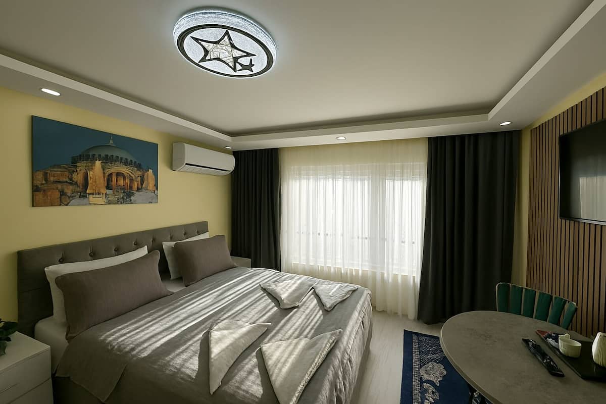 A hotel room with a large bed, a flat-screen TV, a painting on the wall, and a ceiling light fixture.