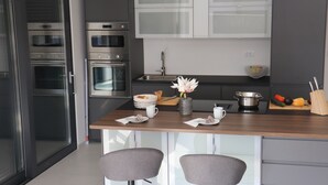A modern kitchen with stainless steel appliances, a wooden countertop, and two bar stools. - Luxusvilla Meerbrise Neu 150m Luftlinie vom Meer (Banjole)