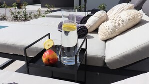 Un verre d’eau avec des tranches de citron et une pomme, posés sur un plateau à côté d’un canapé où se trouvent des serviettes enroulées et un coussin moelleux.