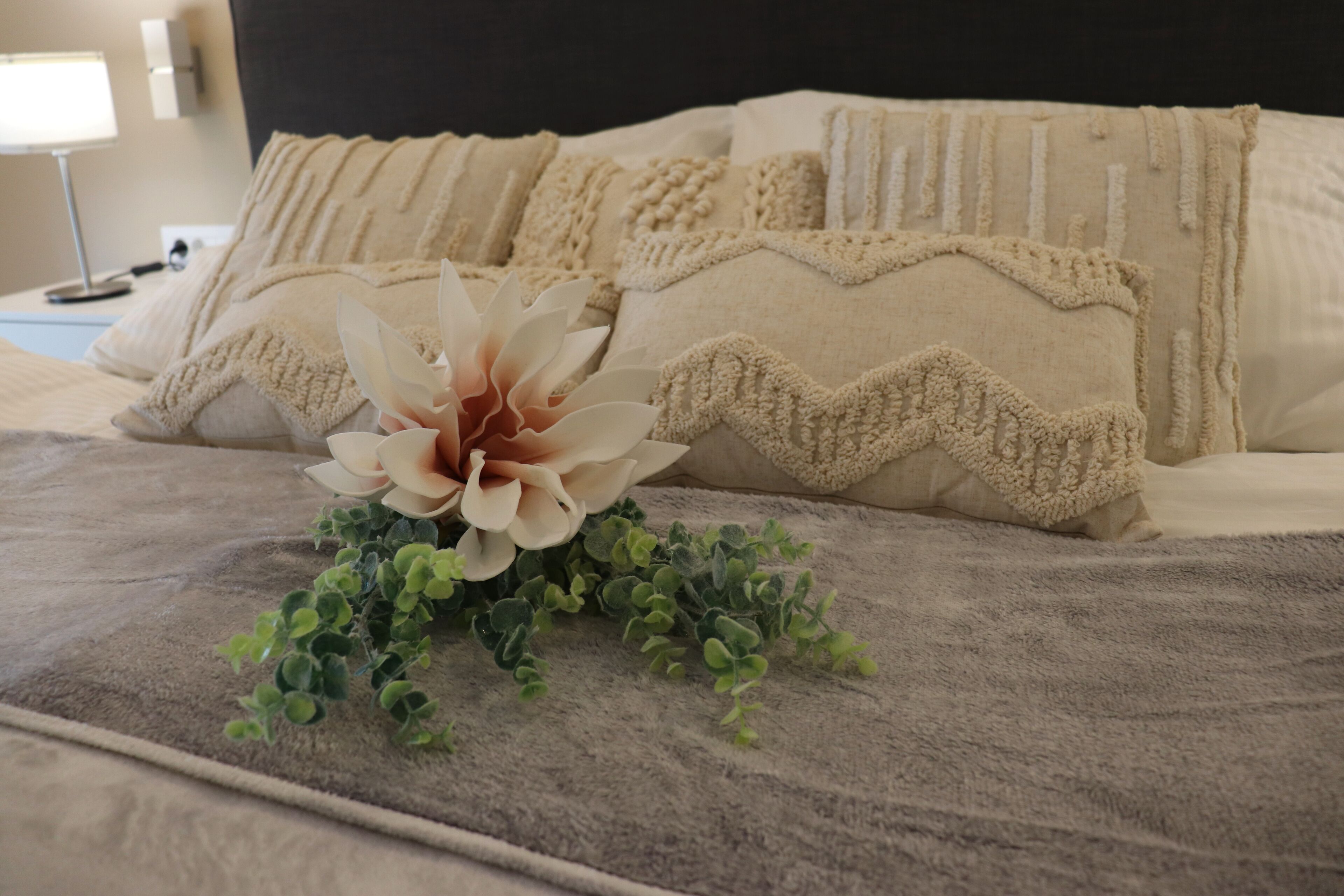 A neatly made bed with a decorative pillow arrangement and a floral accent.