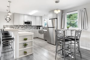 Une cuisine moderne avec des armoires blanches, des appareils en acier inoxydable et un coin bar équipé de tabourets.