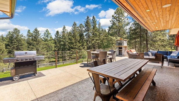 Un patio al aire libre con una parrilla de carbón, una chimenea de piedra, muebles de mimbre y vistas a un bosque.