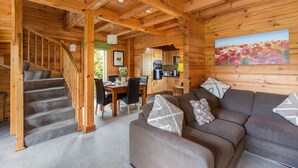 L’intérieur d’un chalet en bois comprend un escalier, un coin repas, une cuisine et un salon avec un canapé et des coussins.