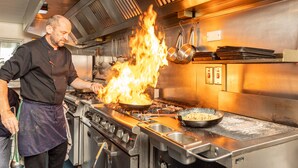 Un chef cuisinant dans une poêle sur une cuisinière, avec des flammes.