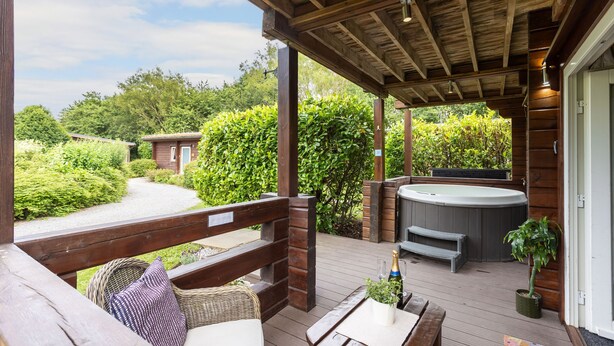 Une terrasse en bois avec un jacuzzi, un espace salon et un chemin menant à une maison.