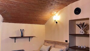 A bedroom with a wooden ceiling, a bed with a headboard, a wall clock, shelves with decorative items, and a small rug. - Florence Cave House (Firenze)