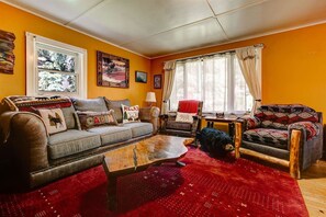 Uma sala de estar aconchegante com sofá, poltrona e mesa de centro, uma janela com cortinas e um tapete vermelho.