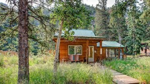 A cabin with a wooden exterior, a metal roof, and a porch with seating. - Riverside`s Hideout Cabin- With Hot Tub! (Lyons)