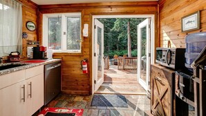 A cabin interior with a kitchen, a dining area, and a deck. - Riverside`s Hideout Cabin- With Hot Tub! (Lyons)
