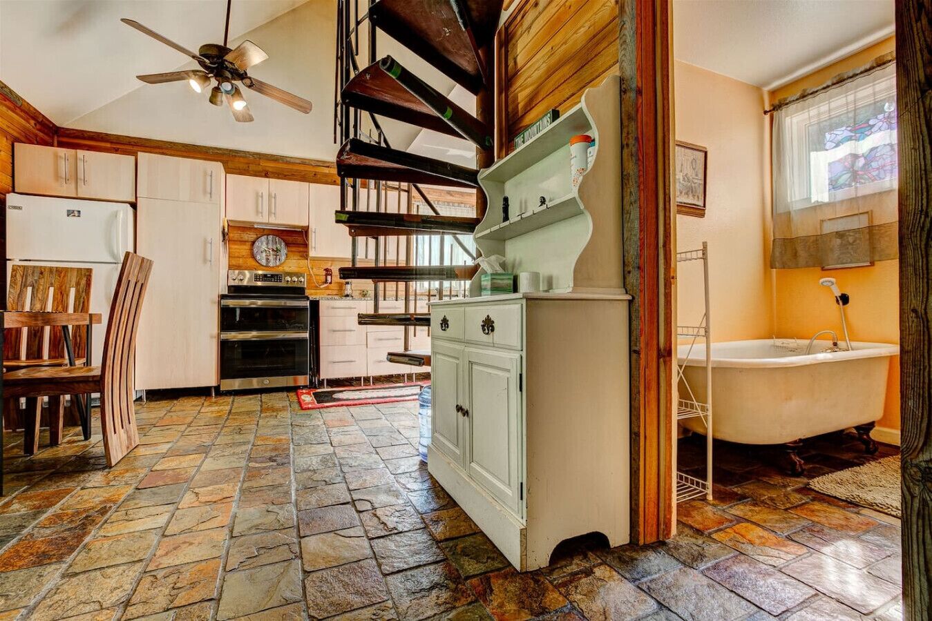 A kitchen with a stone floor, wooden cabinets, a built-in oven, and a ceiling fan.