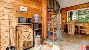 A cabin interior with a wooden interior, a spiral staircase, a dining area with wooden chairs, a microwave, and a water dispenser. - Riverside`s Hideout Cabin- With Hot Tub! (Lyons)