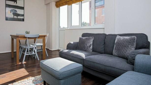Un salon moderne avec un canapé gris, un pouf assorti et une table à manger avec des chaises.