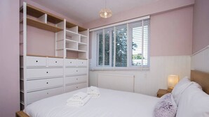 Une chambre à coucher comprenant un lit, une armoire intégrée, une fenêtre avec des stores et une lampe de chevet.