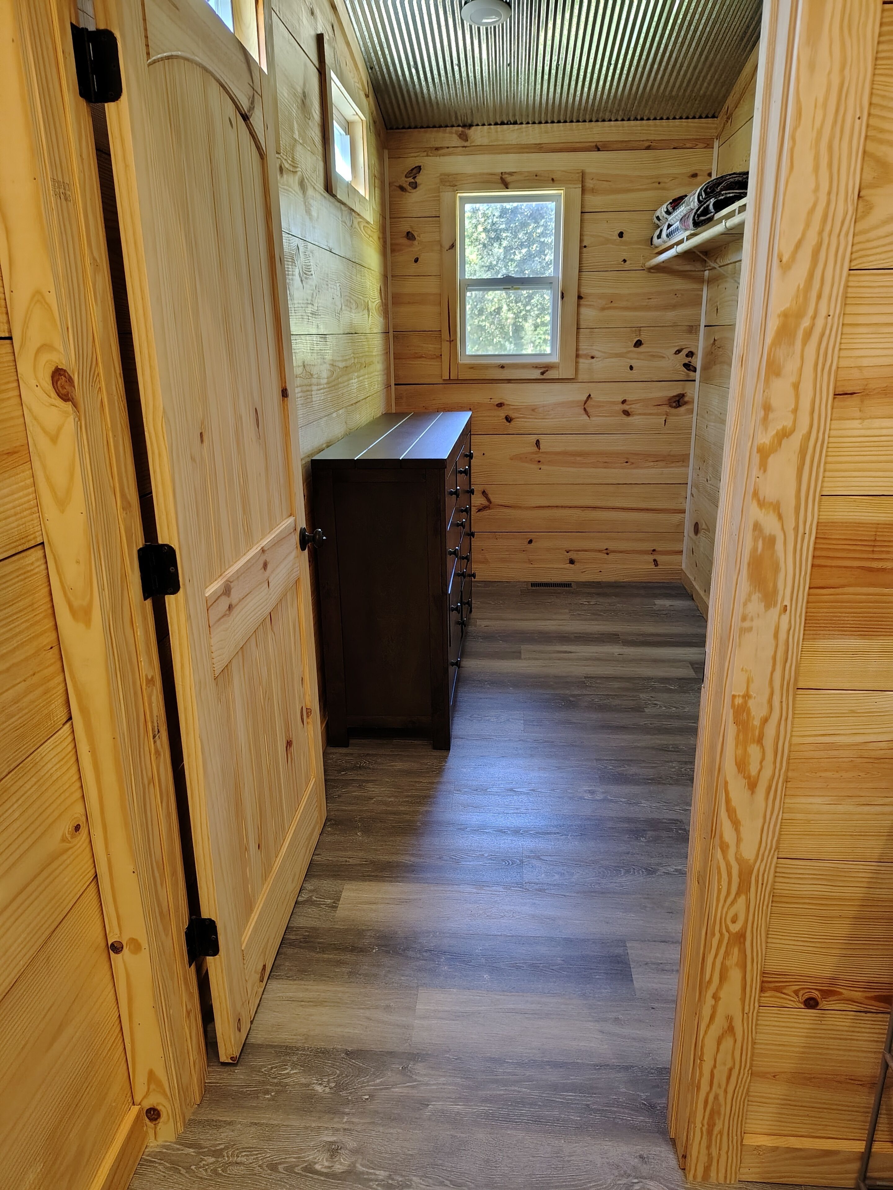 A narrow wooden hallway with a small window, a wooden cabinet, and a door.