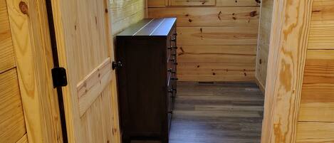 A narrow wooden hallway with a small window, a wooden cabinet, and a door.