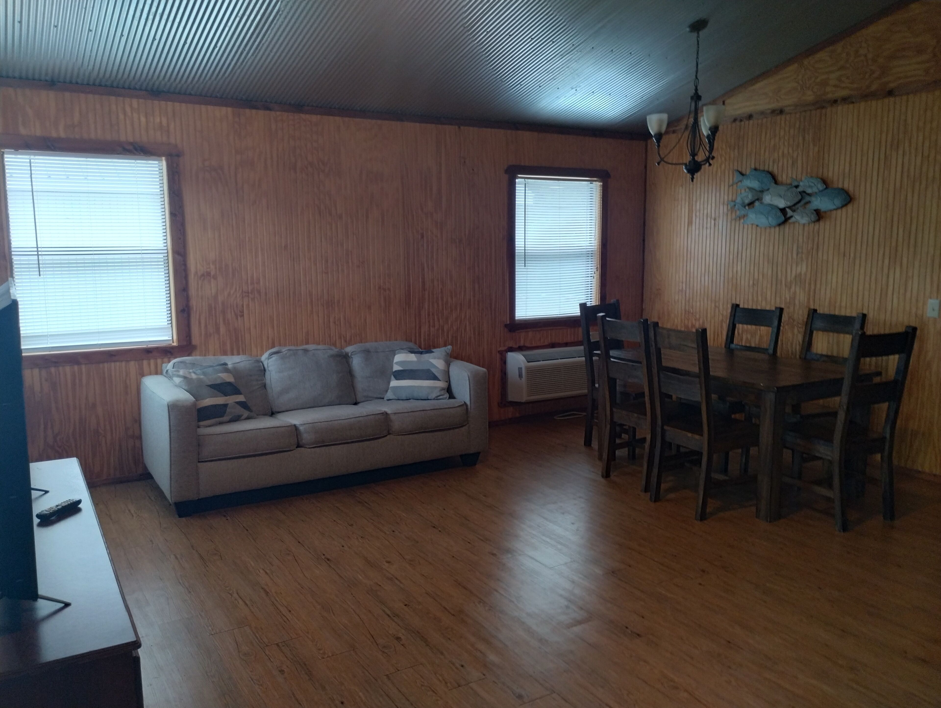 A living room with a sofa, dining table, chairs, and a TV.