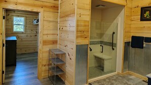 A wooden cabin bathroom with a shower, a small shelf, and a window. - Anglers Riverfront Cabins (Mountain View)