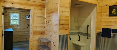 A wooden cabin bathroom with a shower, a small shelf, and a window.
