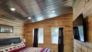 A wooden cabin bedroom with a bed, two windows, and a ceiling with recessed lighting. - Anglers Riverfront Cabins (Mountain View)