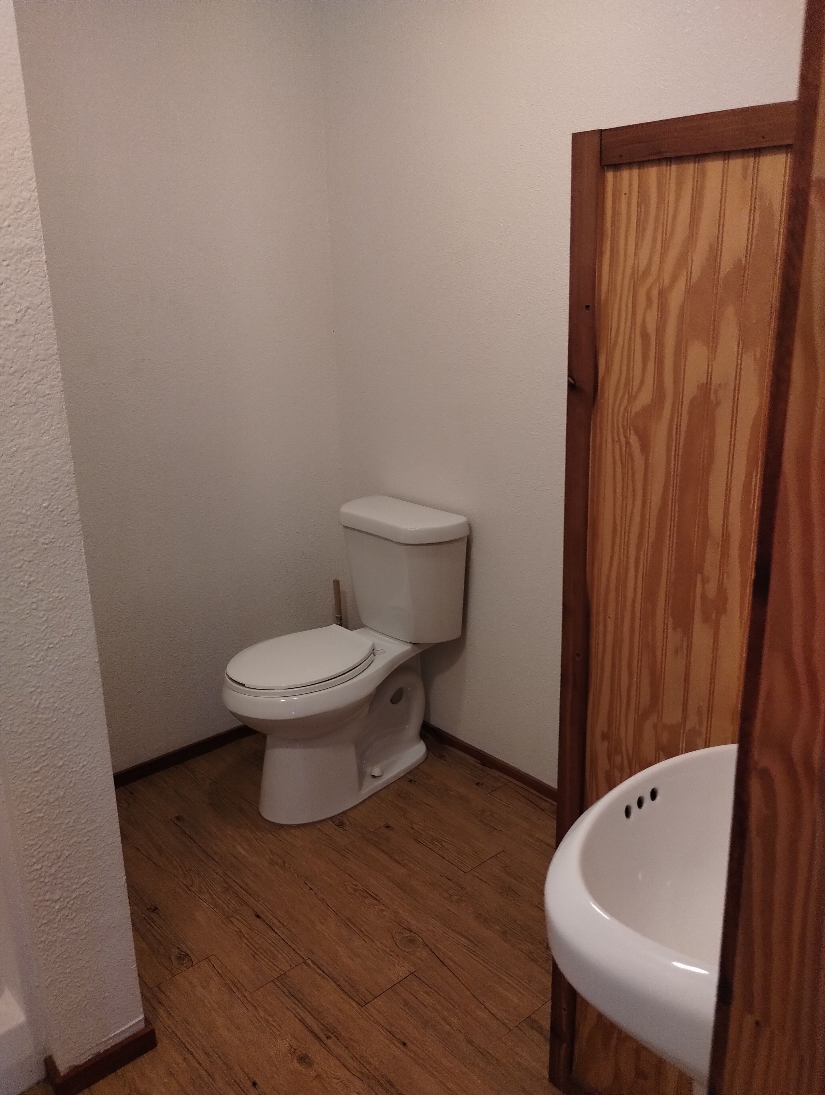 Une petite salle de bain compacte avec des toilettes blanches, un plancher en bois et une porte en bois.