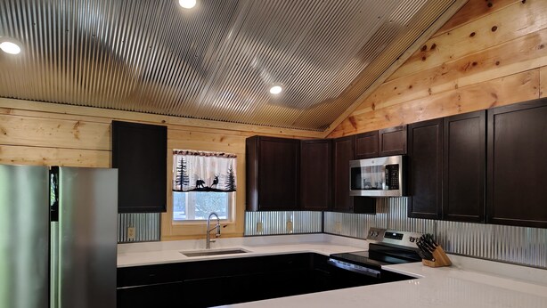 A modern kitchen with wooden panel walls, stainless steel appliances, and a large island. - Anglers Riverfront Cabins (Mountain View)