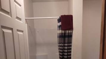 Een douche met een gestreept gordijn en een rode handdoek hangend aan een witte handdoekhouder.