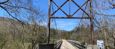 A metal bridge with a concrete walkway, surrounded by trees and hills.
