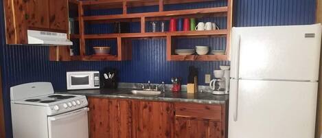 Una cucina compatta con mobili in legno, un fornello bianco, un forno a microonde e un frigorifero.