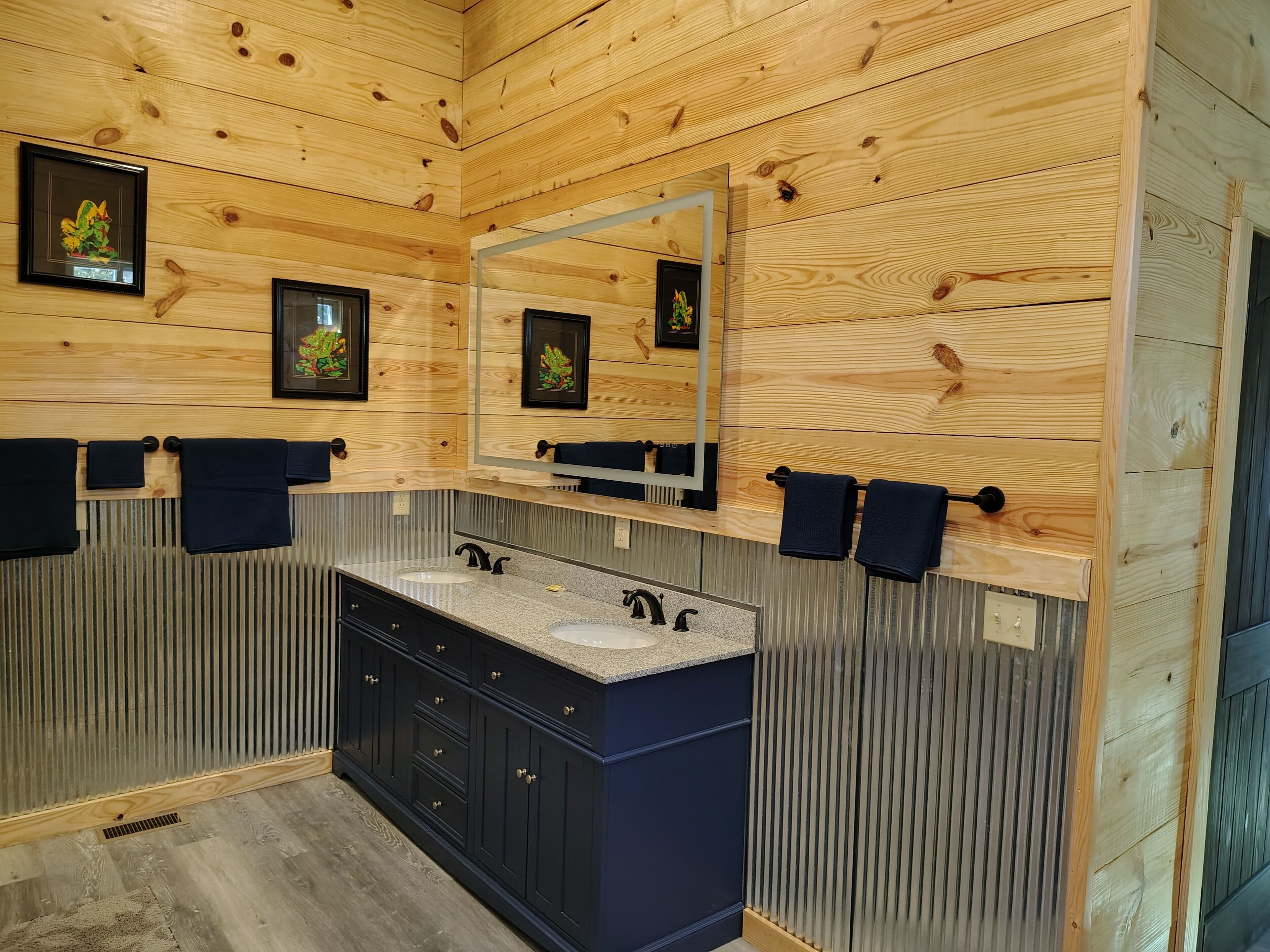 A wooden-paneled bathroom with two sinks, a large mirror, and framed pictures on the wall.