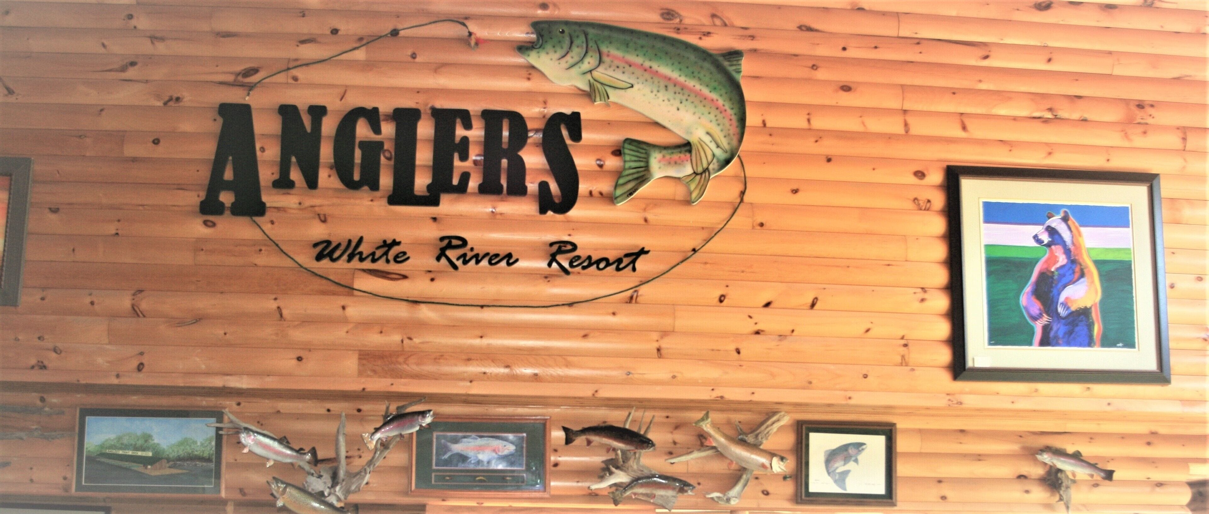 A wooden wall with the sign "Anglers White River Resort" and several framed fish pictures.