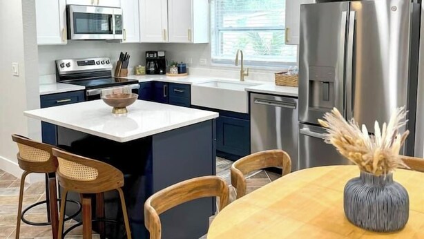 A modern kitchen with white cabinets, stainless steel appliances, and a central island with seating. - Modern Boho- 4/3-King Beds/Pool! Pet friendly! (Tampa)