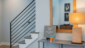 A modern interior with a staircase, a welcome sign, a mirror, and a lamp.